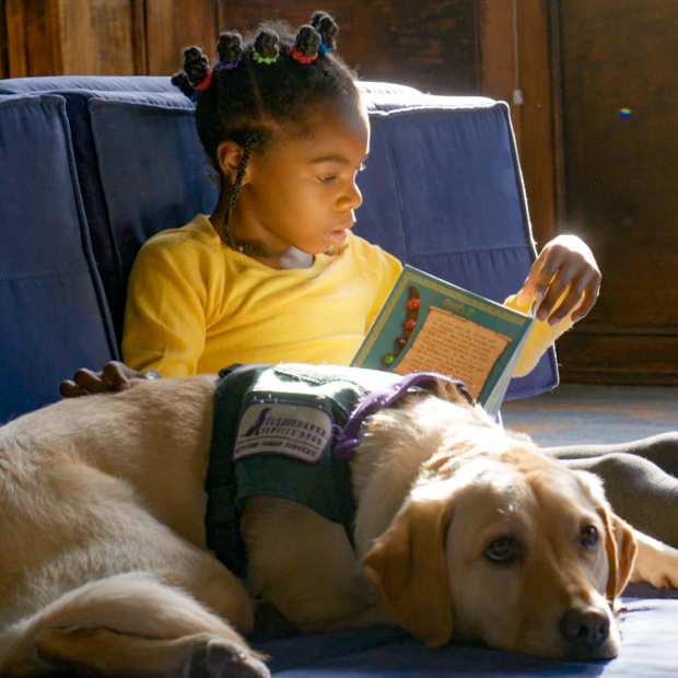 Elementary student sitting on the floor with Bingo the dog reading a book