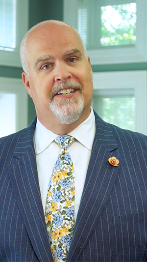 Vertical still of Bob Lane standing in a suit