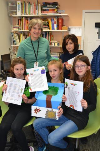 group of students sitting holding up papers with smiling teacher