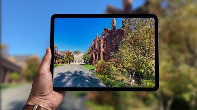 Man holds up iPad in front of beautiful Lab campus to show campus